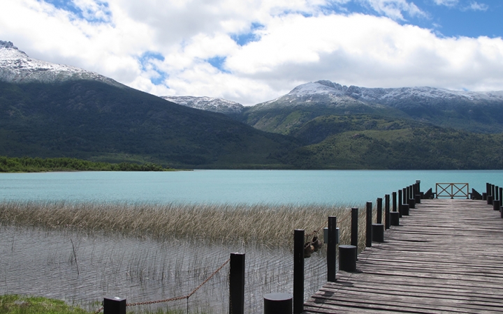 A stock stretches out over a blue body of water. Beyond the water, there are mountains. 